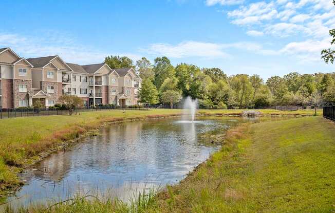 A fountain in the middle of a pond in front of apartment buildings.