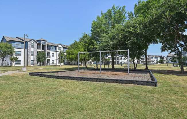 a park with a swing set and trees in front of an apartment building