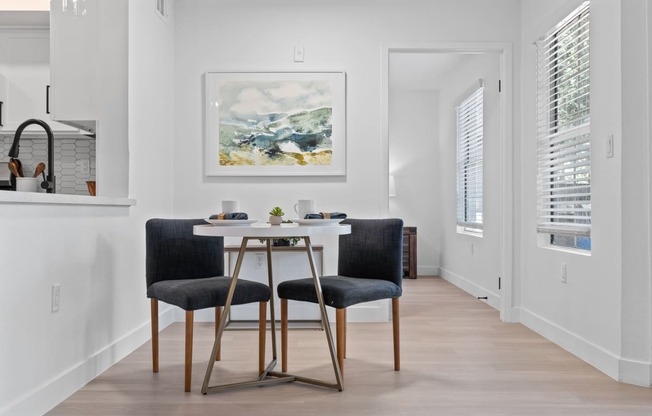 a dining room with a white table and two black chairs
