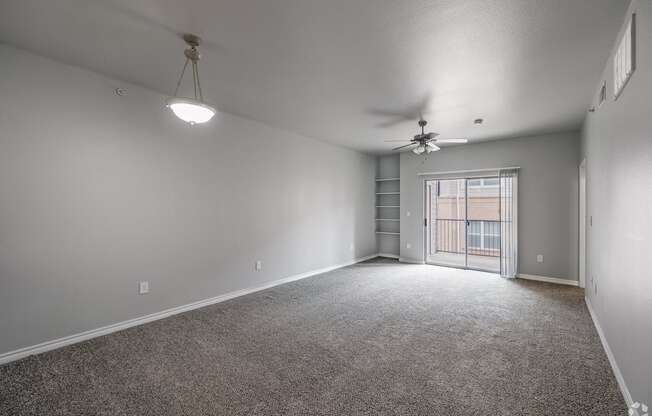 an empty living room with a ceiling fan and a door to a balcony