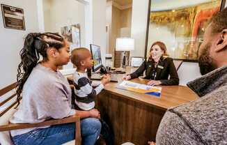 A woman sitting at a desk talking to a family at a reception desk at Confluence at Harvest  Hills.