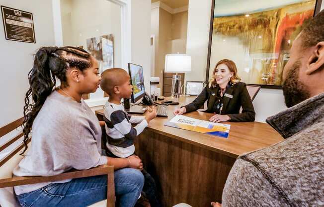 A woman sitting at a desk talking to a family at a reception desk at Confluence at Harvest  Hills.