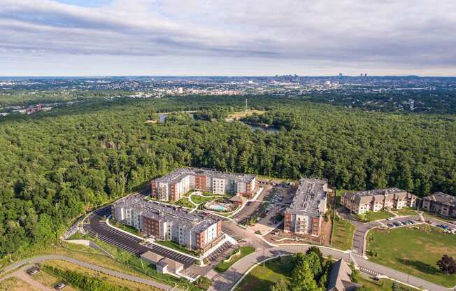 an aerial view of an apartment complex with trees and a city in the background