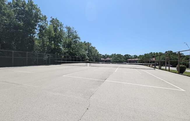 an empty tennis court in a park with trees