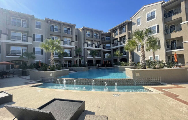 A swimming pool surrounded by a concrete patio and a building with balconies.