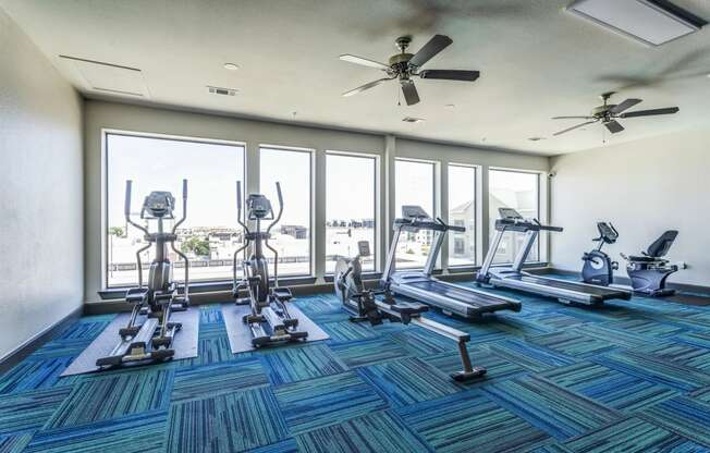 a gym with cardio equipment and large windows with a view of the water