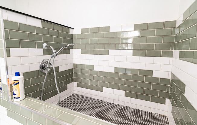 A shower area with a green tiled wall and a white shower head.