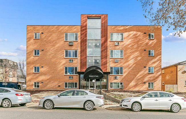 Charming brick apartment building with modern windows and inviting entrance, located at 2444 S. York, with convenient parking and clear blue sky backdrop.