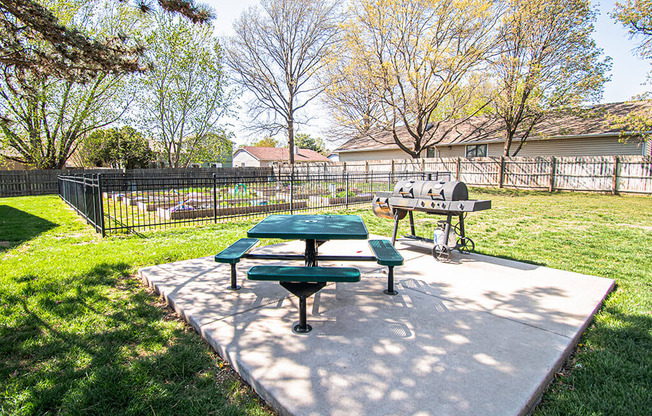 A green picnic table and bench are in a sunny park.