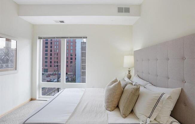 A bedroom with a large bed and a view of a cityscape through the window.