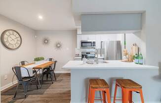 A kitchen with a table and chairs in the foreground and a clock on the wall.
