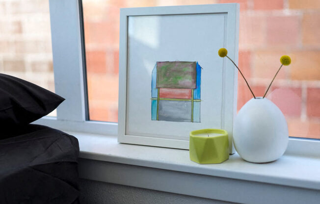 a painting sitting on top of a window sill next to a vase