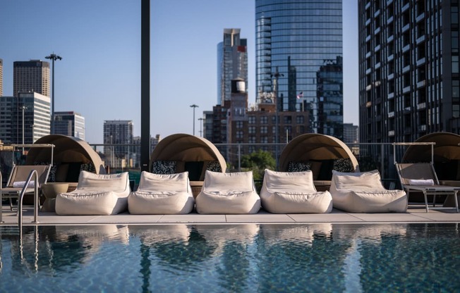 an outdoor pool with white lounge chairs and a city skyline in the background