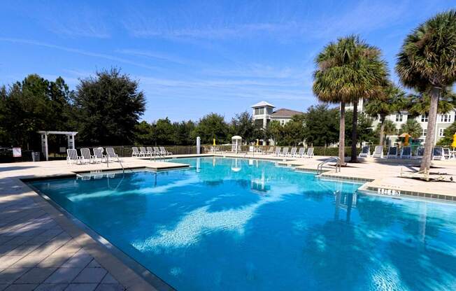A large swimming pool with a white fence and chairs around it.