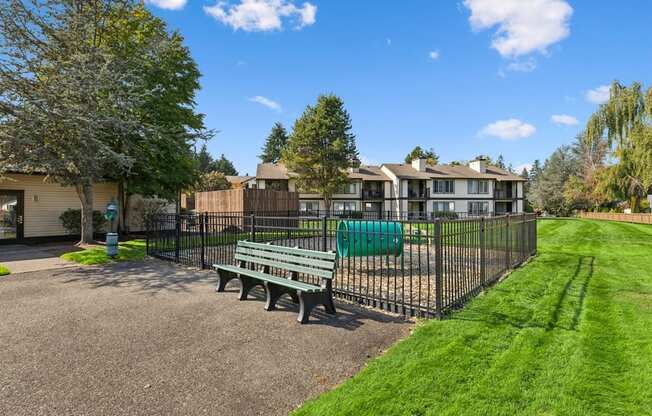 A sunny day at a park with a bench and a fence.