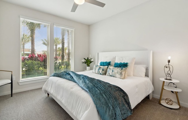 A bedroom with a bed, a fan, and a window with blinds.