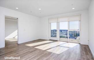 A room with unaltered wooden flooring and a view of the city through the windows.