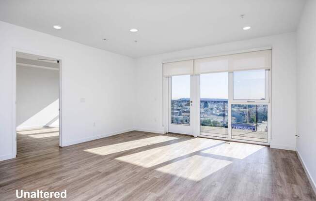 A room with unaltered wooden flooring and a view of the city through the windows.