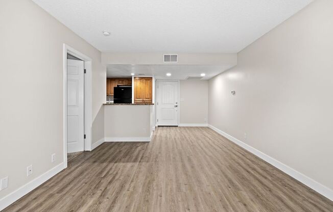an empty living room with a kitchen in the background