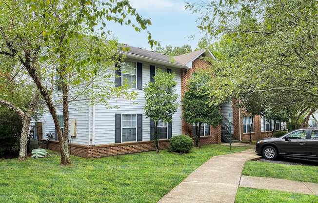 a white and brick house with trees and a sidewalk