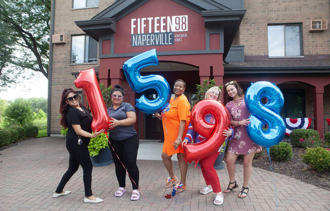 a group of women standing in front of a building holding blue and red balloons that spell out