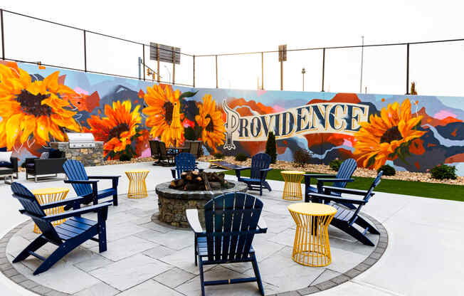 a patio with blue chairs and yellow tables and a fire pit