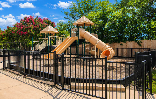 A playground with a yellow slide and a black fence.