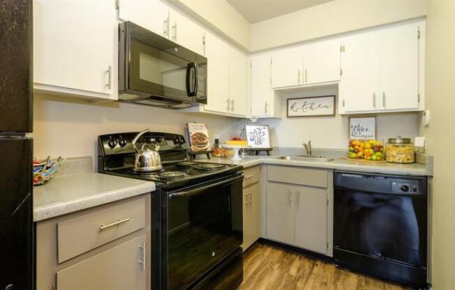 Apartments for Rent Mesa, AZ - Mesa Station - L-Shaped Kitchen with White and Grey Cabinetry, Black Appliances, and Granite-Style Countertops