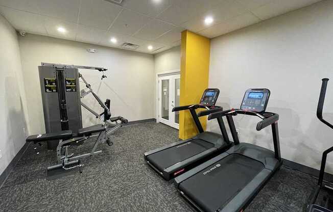 A gym with treadmills, a weight machine, and a yellow wall.