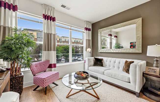 A living room with a white couch, a coffee table, and a large window with curtains.