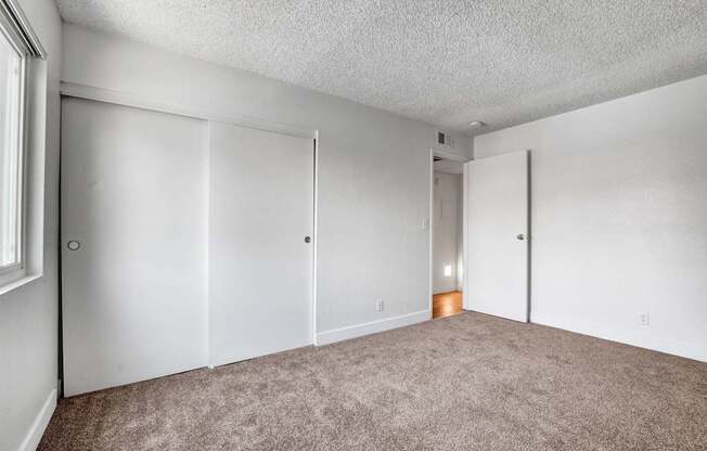 A room with carpeted floor and white walls with a door on the left.