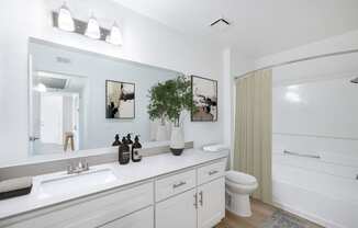 a bathroom with white cabinets and a white toilet next to a white bathtub with a shower