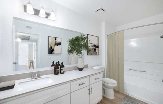 a bathroom with white cabinets and a white toilet next to a white bathtub with a shower