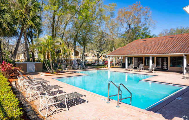 A pool surrounded by chairs and trees.