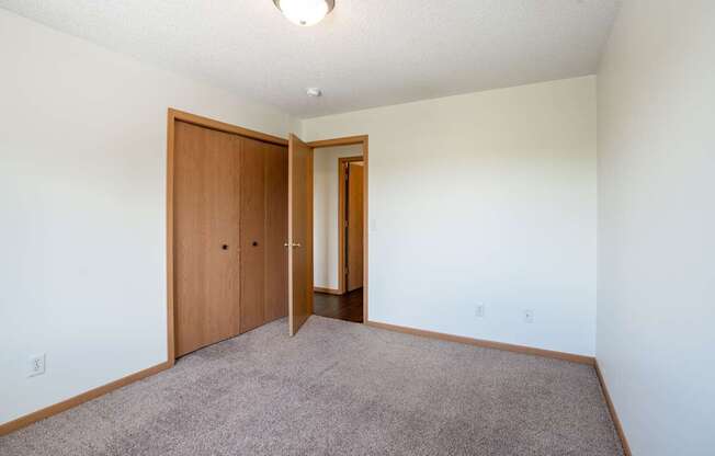 A room with a carpeted floor and two wooden doors. Bismarck, ND Sierra Ridge Apartments