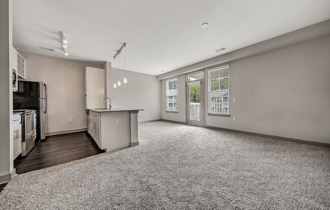 an empty living room with a kitchen and a large window