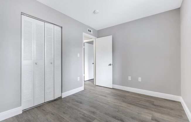 an empty room with white closet doors and a door to a hallway