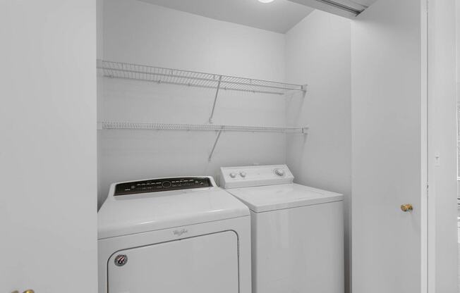 a washer and dryer in a white laundry room with shelves