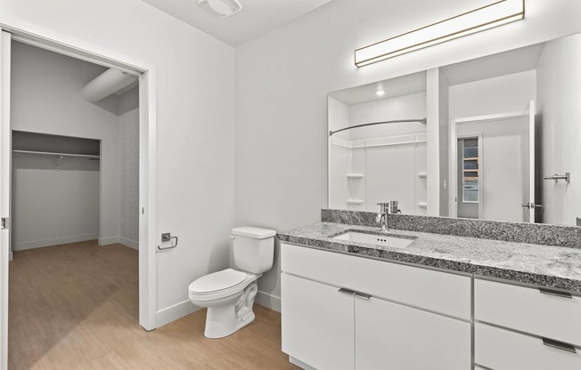 A bathroom with a toilet, sink, and mirror. at Brickside Heights, Millcreek, UT, 84106