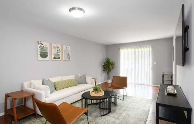 A living room with a white couch, a brown chair, a black table, and a flat-screen TV mounted on the wall.