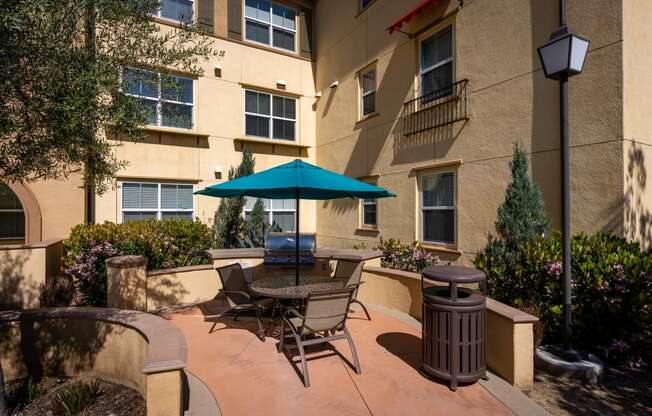 a patio with a table umbrella and chairs in front of an apartment building