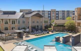 A large swimming pool surrounded by lounge chairs and umbrellas in front of a building.