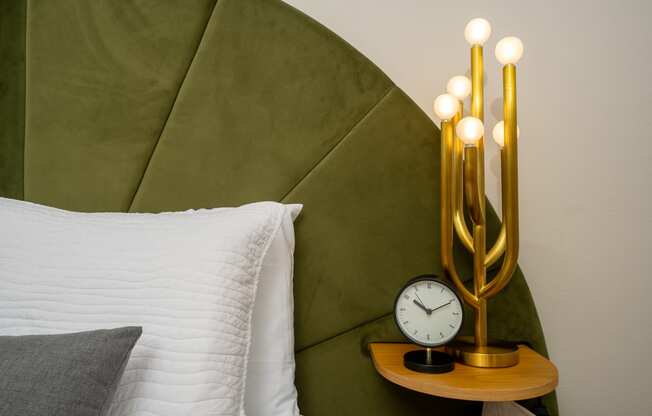 a bed with a white pillow and a green blanket next to a nightstand with a clock