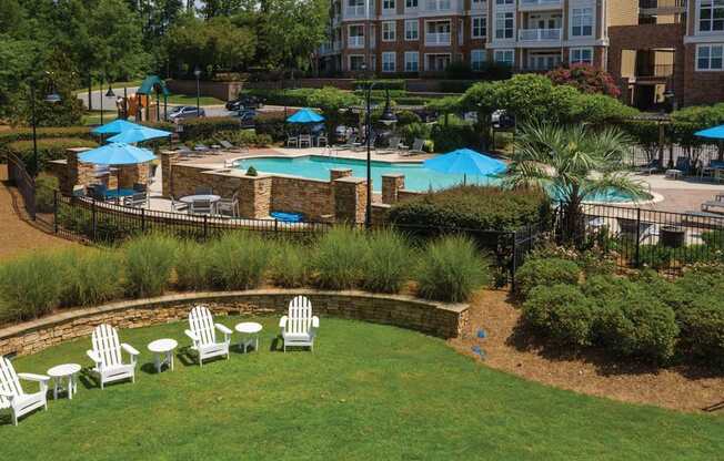 A pool surrounded by a grassy area with chairs and umbrellas.