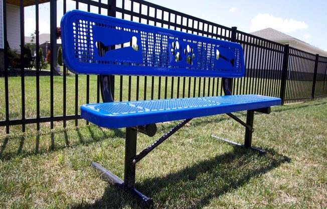 a blue bench in the grass in front of a fence