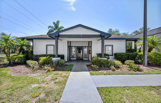 Charming white house with a welcoming entrance, surrounded by lush greenery and vibrant plants, under a clear blue sky.