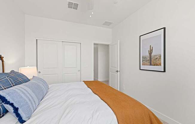 A bedroom with a bed, a lamp, and a picture of a cactus on the wall.