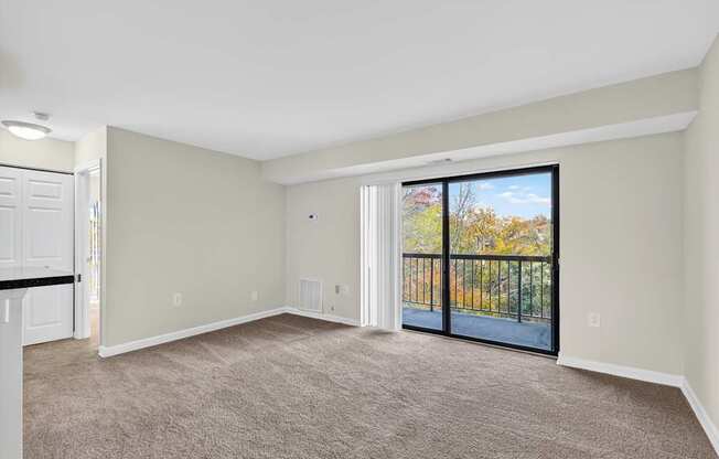 A spacious room with a carpeted floor and a sliding glass door leading to a balcony.