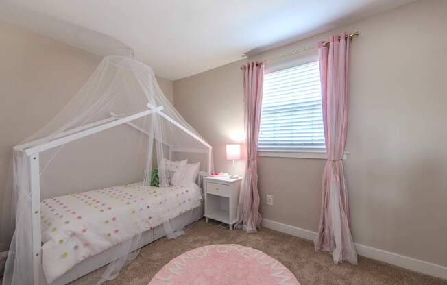 A white bed with a canopy and a pink rug in the middle of the room.