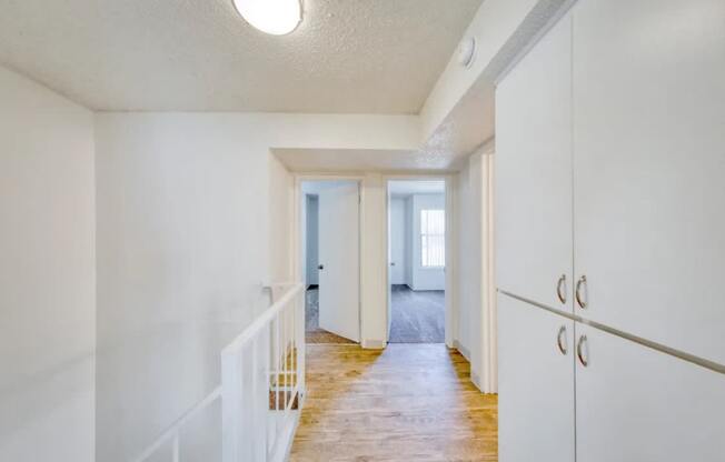 A long hallway with a white railing on the left and a white door on the right.